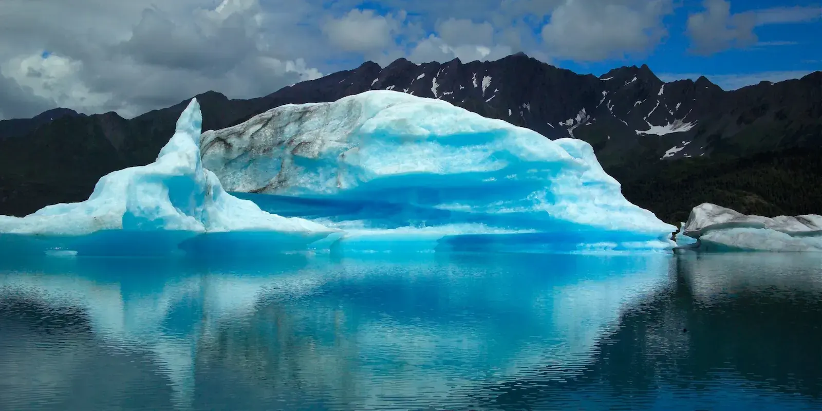A blue iceberg floating beneath Alaska mountains
